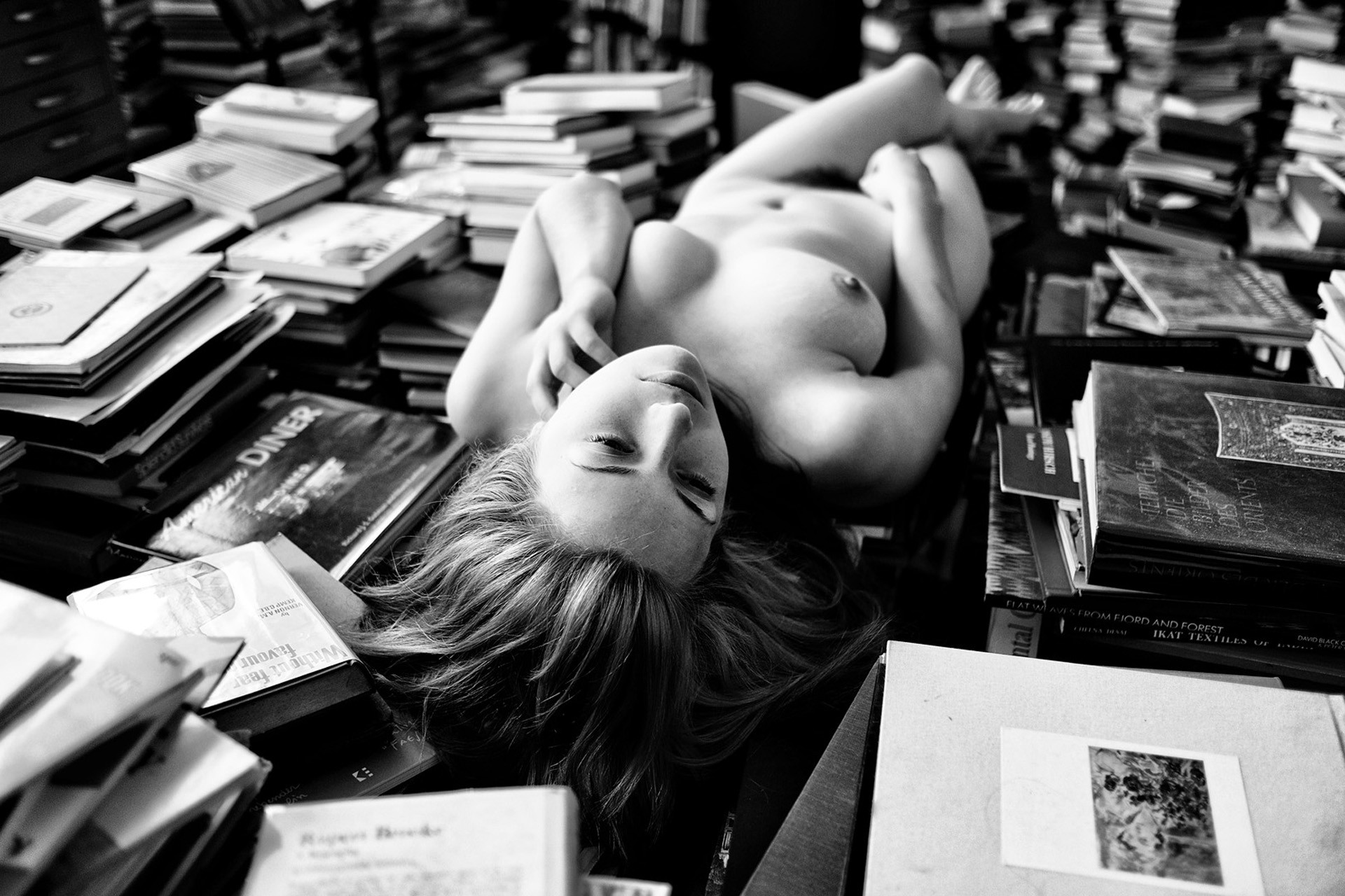 Photographie de nu artistique en noir et blanc, dans une bibliothèque.